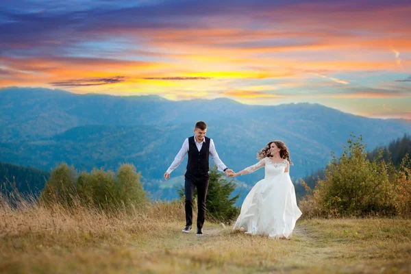 Feliz novia hermosa y elegante novio ejecutar y divertirse, pareja de boda, ceremonia de lujo en las montañas con vista increíble — Foto de Stock