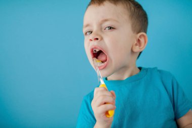 Küçük şirin çocuk mavi arka planda dişlerini fırçalıyor.