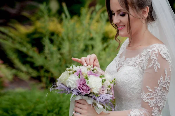 Menyasszony egy ruha áll egy zöld kertben, és gazdaság egy esküvői csokor virágok és zöldség — Stock Fotó