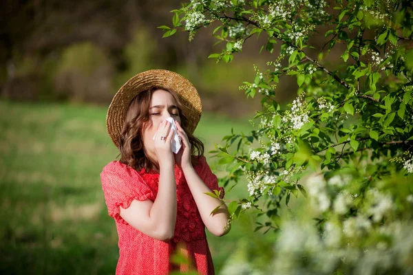 Młoda dziewczyna dmucha w nos i kicha w chusteczkę przed kwitnącym drzewem. Alergeny sezonowe wpływające na ludzi. Piękna pani ma nieżyt nosa.. — Zdjęcie stockowe