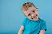 Egy vicces szemüveges, mosolygós kisfiú portréja. Iskola. Óvoda. Divatot. Stúdió portré kék háttérrel, másolás tér