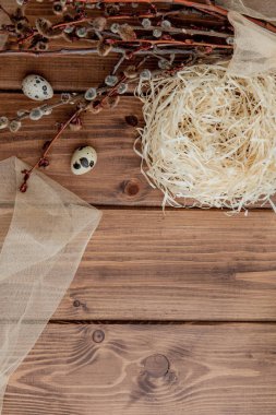 Easter quail eggs in nest and willow branch on a wooden backgrou