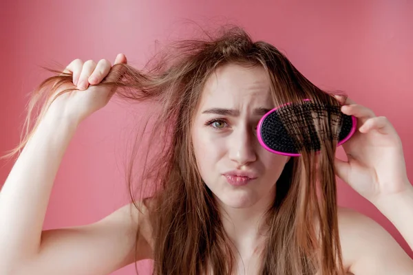 Menina bonita nova que tem problemas enquanto o cabelo no fundo rosa — Fotografia de Stock