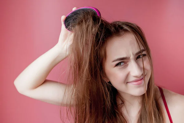 Menina bonita nova que tem problemas enquanto o cabelo no fundo rosa — Fotografia de Stock
