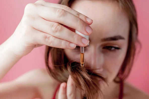 Menina segura em sua mão as pontas de seu cabelo e sua mão direita aplica-los óleo amarelo . — Fotografia de Stock