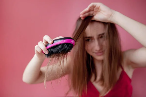 Menina bonita nova que tem problemas enquanto o cabelo no fundo rosa — Fotografia de Stock