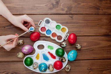 Paskalya yumurtaları, ahşap arka planda boya ve fırçalar. Tatil için hazırlık. Kız elleri bir desen çizer