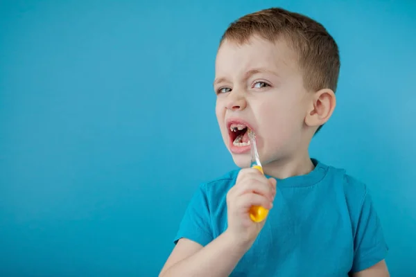 Klein schattig jongen poetsen zijn tanden op blauwe achtergrond — Stockfoto