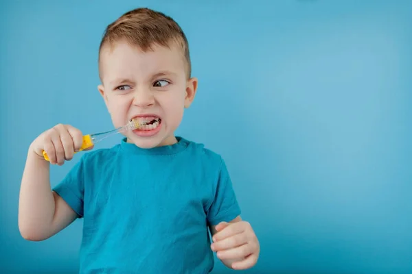 Pequeño chico lindo cepillándose los dientes sobre fondo azul — Foto de Stock