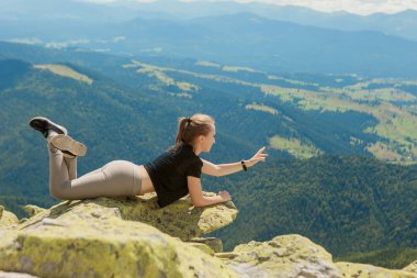 Genç bir kadın bir kayanın üzerinde oturuyor ve ufka bakıyor..