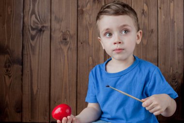 Ahşap arka planda paskalya yumurtası dolu bir sepeti olan mutlu erkek bebek.