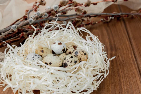 Пасхальные перепелиные яйца в гнезде и ивовая ветвь на деревянном фоне — стоковое фото