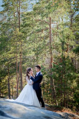 Güzel yeni evliler, kayaların ve dağların arkasında birbirlerine sarılıyorlar. Şık gelin ve güzel gelin uçurumun kenarında duruyor. Düğün portresi. Aile fotoğrafı.