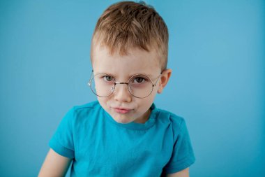 Komik gözlüklü, gülümseyen bir çocuğun portresi. - Okul. Anaokulu. Moda. Mavi arkaplanda stüdyo portresi, boşluğu kopyala