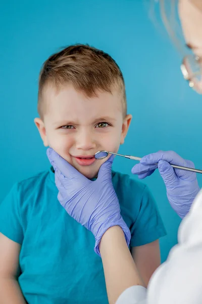 Kleine patiënt wil de mond van de tandarts niet openen op een blauwe achtergrond. Dantist behandelt tanden. close-up uitzicht op tandarts behandeling tanden van kleine jongen in tandarts kantoor. — Stockfoto