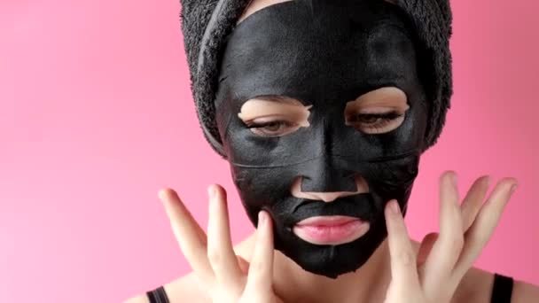 Young Woman Apply Black Cosmetic Fabric Facial Mask Pink Background — Stock Video