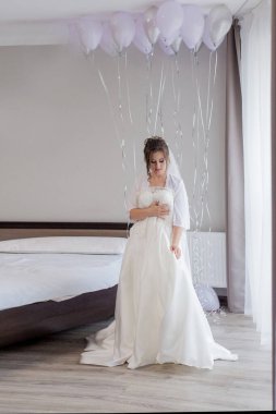 İpek bornozlu genç kadın gelinliğine dokunuyor ve pencerenin yanında dururken gülümsüyor. Düğün günü. Güzellik, moda. En mutlu düğün günü. Her anın tadını çıkar