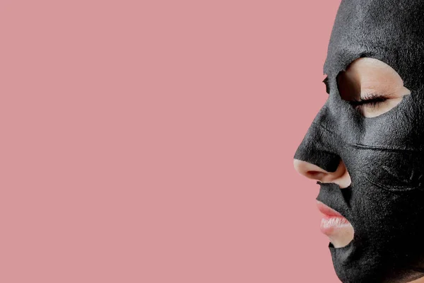 Jovem Mulher Aplicar Máscara Facial Tecido Cosmético Preto Fundo Rosa — Fotografia de Stock