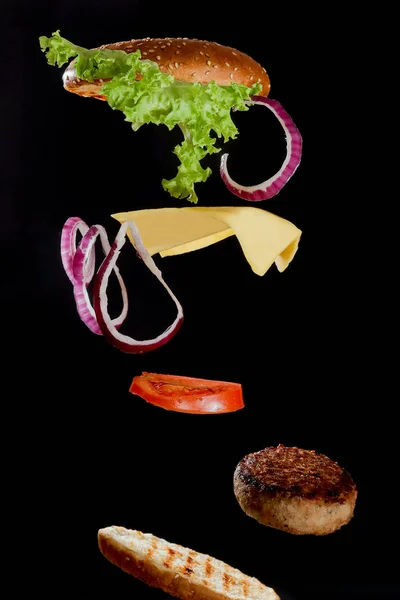 Flying ingredients burger or cheeseburger on a small wooden cutting board isolated on a dark background. Burger floating in the air above the table. Space for text.