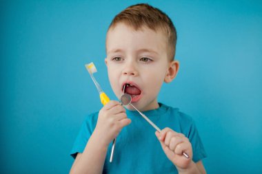 Küçük şirin çocuk mavi arka planda dişlerini fırçalıyor..