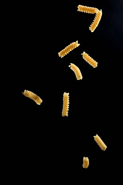 Spadające makaronu fusilli. Latający żółty surowego makaronu na czarnym tle — Zdjęcie stockowe