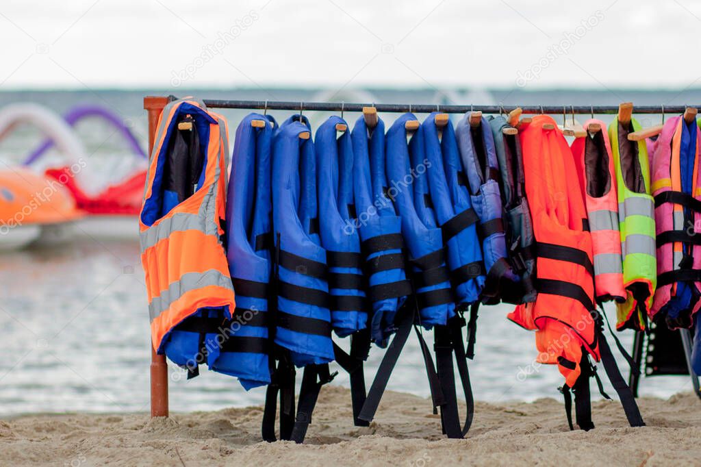 Close-up group of Life jackets or life vests hanging on the wall of the boating station against sea coast.