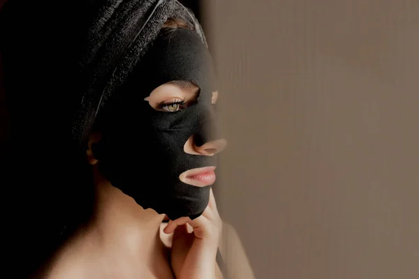 黒い顔のマスクを適用する美しい女性 美容トリートメント 黒の背景に粘土顔のマスクを適用スパガールのクローズアップ肖像 — ストック写真