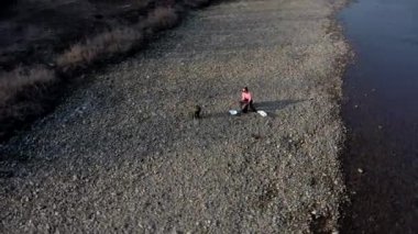 Oğluyla birlikte genç bir kadın nehirdeki bir çöp torbasında plastik çöp topluyor. Kullanılmış kirli plastik şişeler. Çevre kirliliği kıyısı