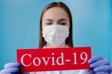 Cerrahi maskeli doktor kadın mavi arka planda kurtarıcı Coronavirüs olan kırmızı kağıda işaret ediyor. Dünya Sağlık Örgütü WHO, COVID-19 adlı Coronavirus hastalığına yeni bir resmi isim verdi.