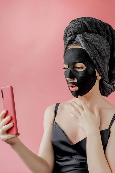 여자들은 분홍빛 배경에 화장품용 마스크를 전화를 숯으로 얼굴벗기기 마스크쓰기 — 스톡 사진