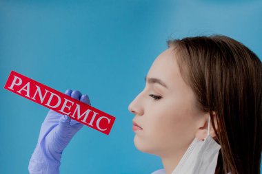 Cerrahi maskeli doktor kadın mavi arka planda kurtarıcı Coronavirüs olan kırmızı kağıda işaret ediyor. Dünya Sağlık Örgütü WHO, COVID-19 adlı Coronavirus hastalığına yeni bir resmi isim verdi.