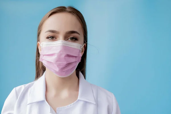 Enfermera doctora sonriendo detrás de máscara de cirujano. Retrato de primer plano de una joven modelo caucásica sobre fondo azul. Mujer usando masa para proteger a covid-19 —  Fotos de Stock