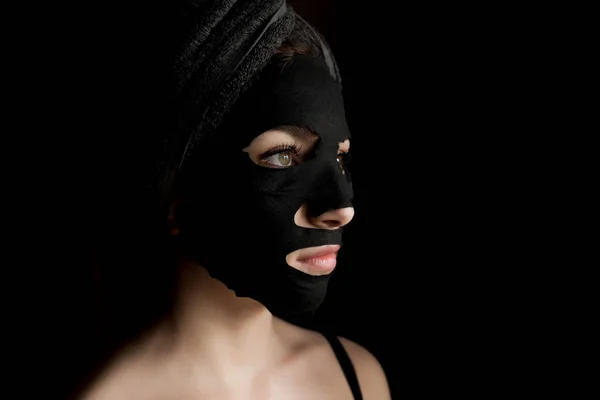 黒い顔のマスクを適用する美しい女性 美容トリートメント 黒の背景に粘土顔のマスクを適用スパガールのクローズアップ肖像 — ストック写真