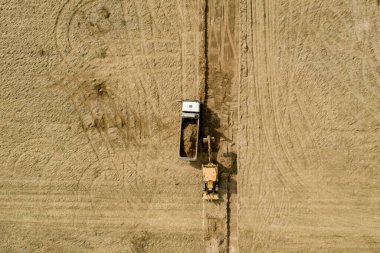 Yükleyici kazıcı zemini yol inşaatındaki kamyona yüklüyor..