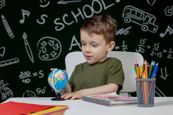 Leuke Slimme Jongen Zit Aan Een Bureau Met Wereldbol Hand — Stockfoto