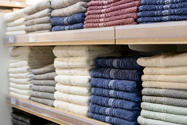 Folded multicolored towels on shelves. Neatly folded clothes. Rack of clothes with warm. Cotton towels neatly folded.