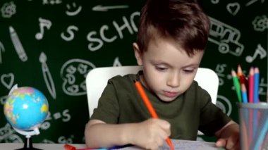 Ev ödevi yapan sevimli çocuk. Masada çizim yapan zeki bir çocuk. Öğrenci çocuk. İlkokul öğrencisi iş yerinde resim çiziyor. Çocuk öğrenmeyi seviyor. Evde eğitim. Okula dönelim. Okuldaki küçük çocuk.