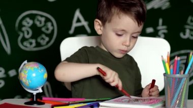 Ev ödevi yapan sevimli çocuk. Masada çizim yapan zeki bir çocuk. Öğrenci çocuk. İlkokul öğrencisi iş yerinde resim çiziyor. Çocuk öğrenmeyi seviyor. Evde eğitim. Okula dönelim. Okuldaki küçük çocuk.