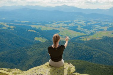 Genç bir kadın bir kayanın üzerinde oturuyor ve ufka bakıyor.
