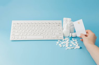 İlaç ve klavyeli alışveriş arabası oyuncağı. Haplar, su toplayan paketler, tıbbi şişeler, termometre, mavi arka planda koruyucu maske. - Evet. Sağlık ve internet alışverişi. Metniniz için en üstteki görünüm.