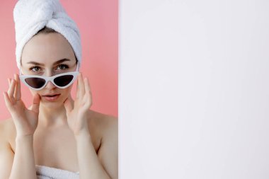 Pembe arka planda banyodan sonra kafasında havluyla gözlüklü güzel bir kadın..