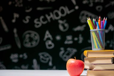 Kitaplar, kalemler ve beyaz masanın üzerindeki elmayla okula geri dön.