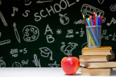 Kitaplar, kalemler ve beyaz masanın üzerindeki elmayla okula geri dön.