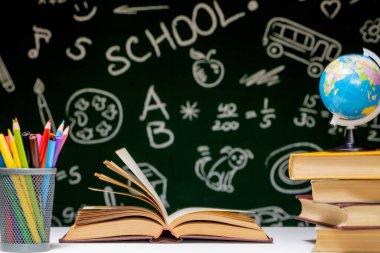 Kitap, kalem ve küre ile okul arka planına yeşil karatahta arka planında beyaz masa üzerinde