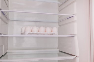 Yumurta tepsisindeki buzdolabının boş rafında duran tavuk yumurtaları..