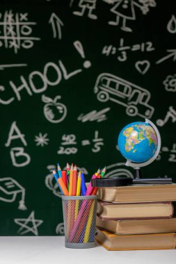 Kitap, kalem ve küre ile okul arka planına yeşil karatahta arka planında beyaz masa üzerinde
