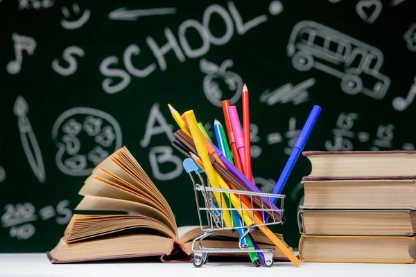 Back to school background with books, pencils and globe on white table on a green blackboard background