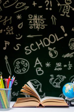 Kitap, kalem ve küre ile okul arka planına yeşil karatahta arka planında beyaz masa üzerinde