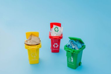 Sarı, yeşil ve kırmızı geri dönüşüm kutularında mavi arka planda geri dönüşüm sembolü var. Şehri düzenli tutar, geri dönüşüm sembolünü bırakır. Doğa koruma kavramı.