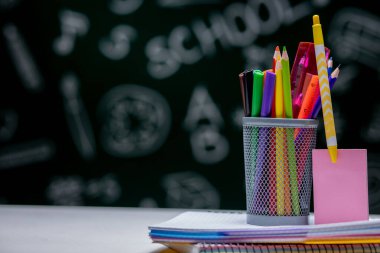 Kırtasiye malzemeleriyle okul geçmişi. Kitap, küre, kalem ve çeşitli ofis malzemeleri yeşil bir karatahta arka planda masanın üzerinde duruyor..